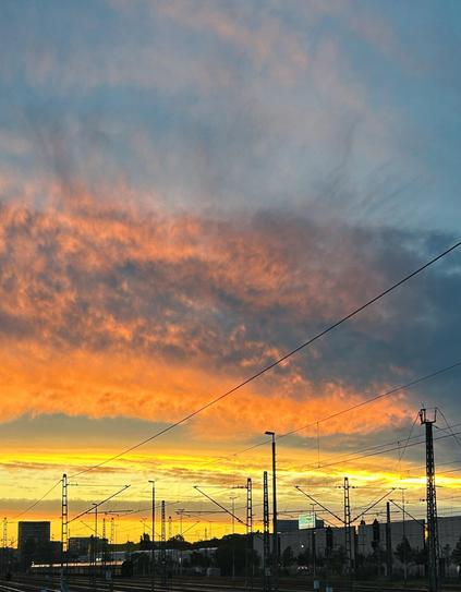 Foto: ein glühender Himmel in strahlendem Gelb, orange und blau. Darunter sind Bahngleise zu sehen.