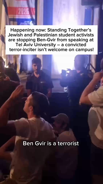 Aufnahme eines Podiums, vor welchem diverse Menschen in weißen Shirts auf dem Boden sitzen und laut rufen. Sie werden von anderen gefilmt. Oben eingeblendet als Text

"Happening now: Standing Together's Jewish and Palestinian student activists are stopping Ben-Gvir from speaking at Tel Aviv University — a convicted terror-inciter isn't welcome on campus!"

Ben-Gvir betritt die Bühne und scheint Richtung Publikum ein Herz mit seinen Händen zu formen. Danach winkt er zu. Die Aktivist*innen stehen auf und werden zusammen/weggedrückt von Sicherheitskräften. Aufnahmen während des Sitzens zeigen sie während sie rufen "We will not let fascism prevail" sowie "Get out of here". Am Ende Einblendung vom Logo von Standing Together.