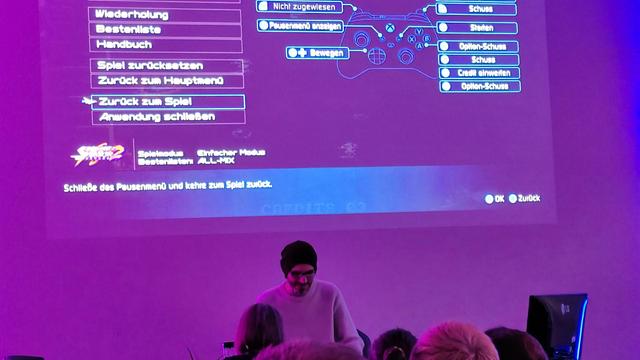 Gregor vor einem pink und blau angeleuchteten, der aus sieht wie ein Gaming-Menu.